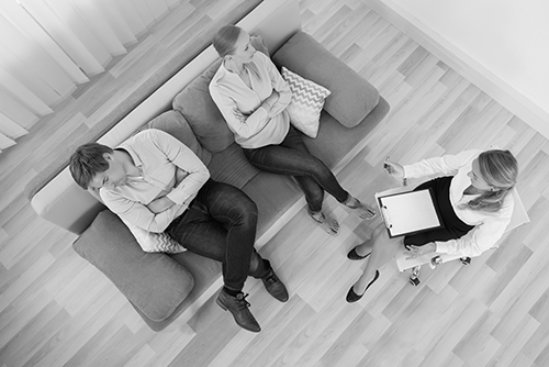 Unhappy Couple Sitting With Psychologist At Home